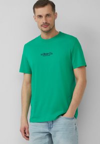 Groene katoenen t-shirt met een ronde hals, korte mouwen en een voorprint met "s.Oliver Co. Opgericht 1969" in zwart.