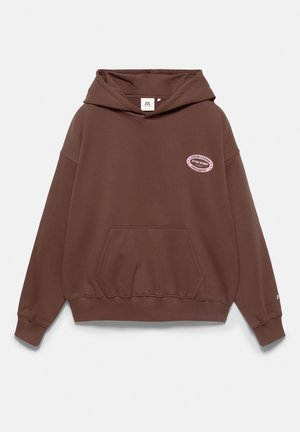 Sweat à capuche marron avec poche avant et capuche, avec un petit patch ovale rose indiquant "Choose courage even when overcomfort" sur la poitrine.