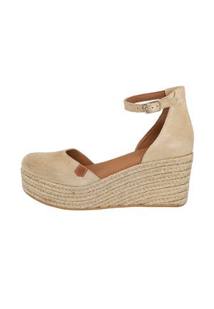 Sandalia de cuña de ante beige con tira ajustable en el tobillo, puntera redonda y plataforma de yute trenzado. Presenta un pequeño acento de logo marrón.