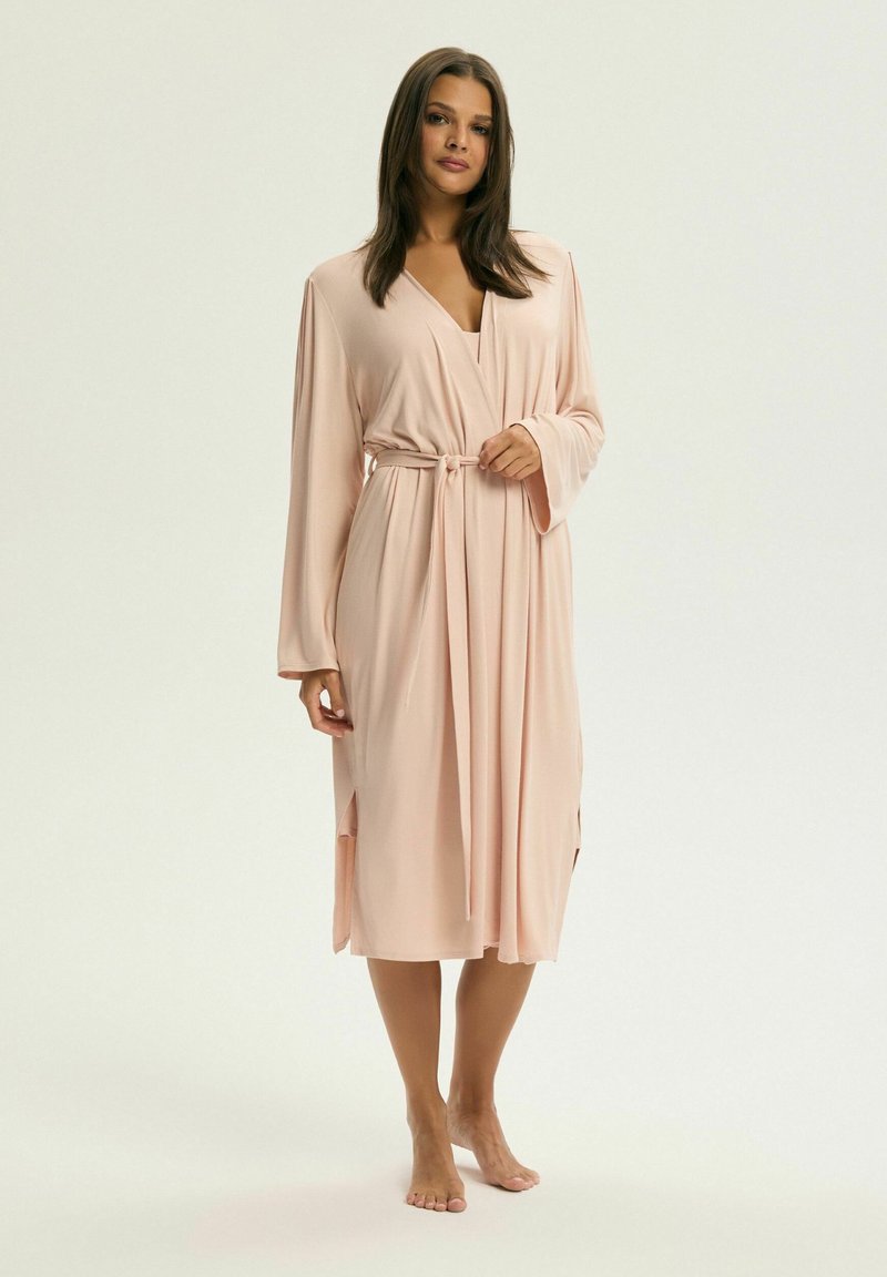 Długi, różowy szlafrok wykonany z gładkiego materiału, z projektem zapinanym na krzyż, długimi rękawami, paskiem w talii oraz bocznymi rozcięciami dla swobody ruchów.