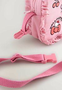 Rosa tygryggsäck med volanger, prydd med körsbärsdesign och Hello Kitty-logotyp. Inkluderar en matchande rosa rem med justerbar klämma.