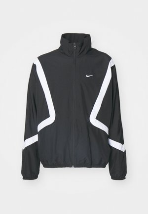 Veste coupe-vent noire avec des rayures diagonales blanches, col haut, fermeture éclair à l'avant, poignets et taille élastiques ; présente un petit logo sur la poitrine.