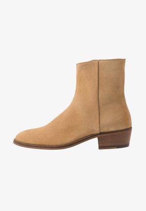 Bottine en suède beige avec un bout arrondi, un petit talon empilé et des côtés sans coutures. Présente une texture lisse et un design minimaliste.