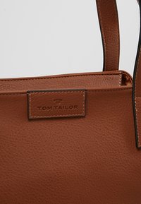 Sac à main en cuir marron texturé avec patch logo cousu marqué "Tom Tailor" et bretelles en cuir assorties.