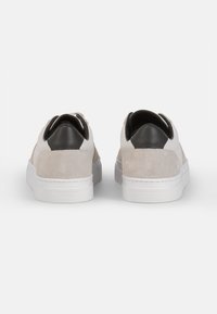 Suede- und Leder-Sneaker im Low-Top-Stil in Hellgrau, mit einer weißen Sohle, schwarzen Fersenelementen und einem minimalistischen Design mit runder Form.