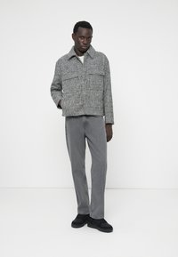 Γκρι καρό, κοντό σακάκι με ανοιχτό γιακά; δύο μπροστινές τσέπες. Συνδυασμένο με γκρι παντελόνι ίσιου κόψιμου και μαύρα sneakers. Λείος υφάς.