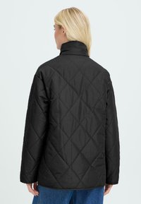 Sort quiltet jakke med høj krave og diamantmønster, med en afslappet pasform og lange ærmer, synlige stikninger og uden synlige lukninger.