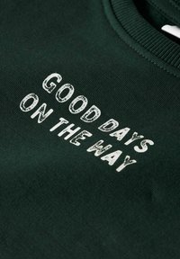 Sweatshirt vert foncé avec un texte en relief blanc "GOOD DAYS ON THE WAY" au fini texturé. Encolure côtelée et tissu doux.
