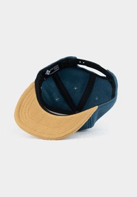 Blaues und sandfarbenes Cap mit einem weichen, strukturierten Schirm. Das Innere zeigt ein schwarzes Futter und klare Luftlöcher. Das Etikett ist hinten sichtbar.