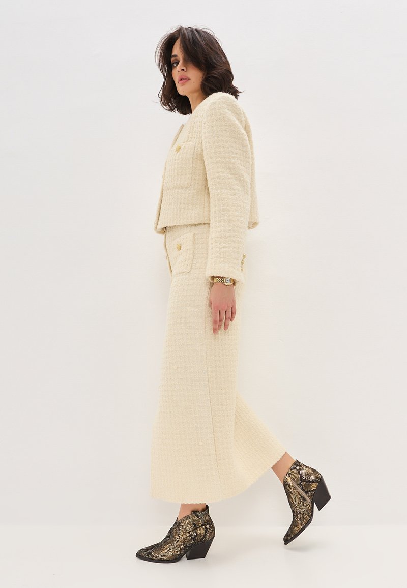 Ensemble coordonné beige texturé avec une veste courte et une jupe longue, associé à des bottines à talons en imprimé serpent noir et doré.