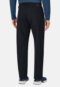 Schwarze Hosen mit geradem Schnitt, ausgestattet mit zwei Gesäßtaschen und einem strukturierten Stoff. Kombiniert mit blauen Schuhen und einem langärmligen Hemd.