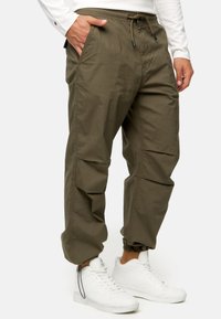 Olivengrønne cargobukser med snoretræk i taljen, sidelommer og elastiske manchetter, lavet af letvægtsstof. Båret med hvide sneakers.
