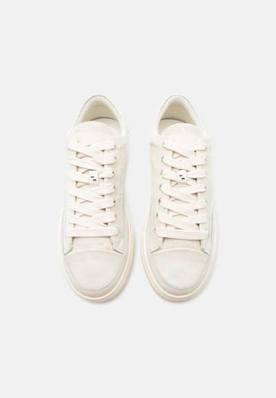 Ζευγάρι παπούτσια τύπου sneakers σε εκρού απόχρωση, χαμηλά, με κορδόνια, λαστιχένιες μύτες και υφασμάτινο επάνω μέρος με υφή, σε προβολή από πάνω σε απλό φόντο.