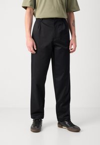 Pantalon noir avec une silhouette droite et une texture lisse. Associé à des baskets noires, mettant en avant un design simple et fonctionnel.