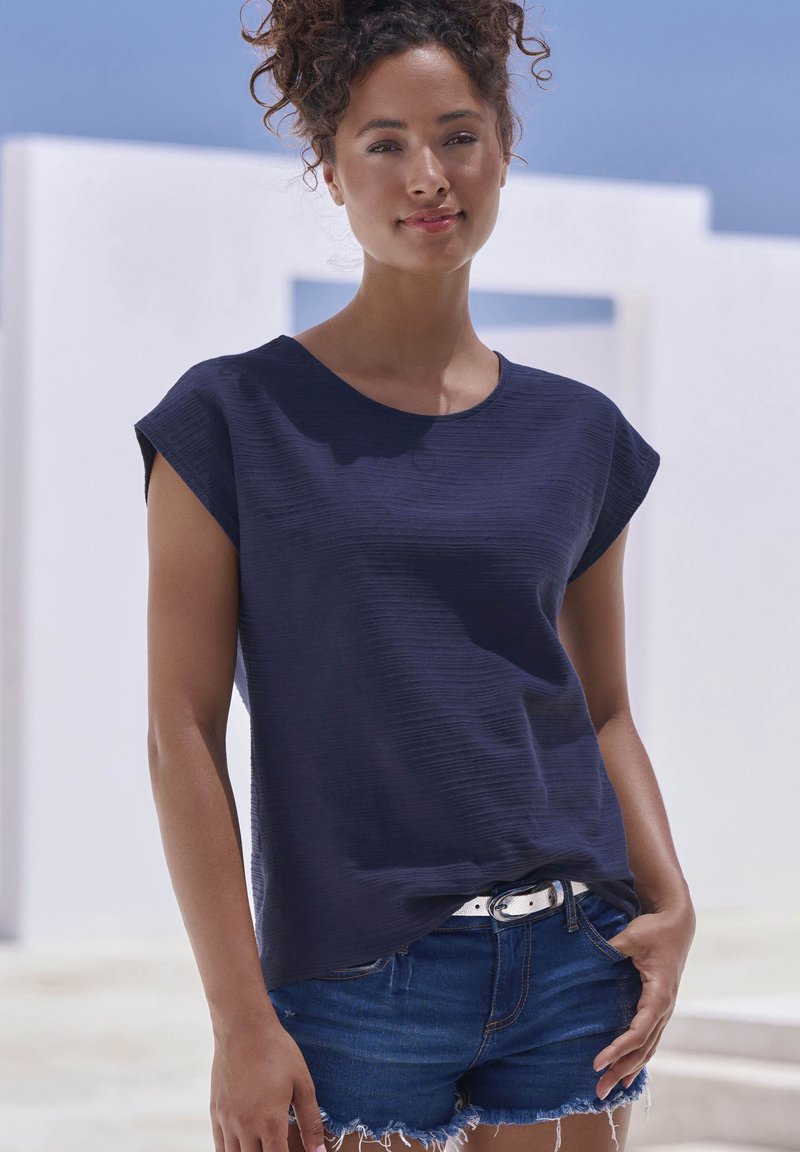 Navy blue short-sleeve top with a textured fabric, round neckline, and relaxed fit, paired with denim shorts featuring frayed hems.