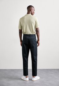 Lys grønn kortermet polo skjorte kombinert med svarte smale bukser og hvite sneakers med brune detaljer. Glatt stofftekstur, skreddersydd passform.