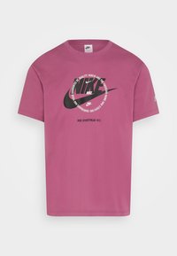 Rosa bomullströja med en stor svart Nike-logotyp i cirkulär design med text, korta ärmar och rundad halsringning.