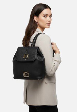 Zaino in pelle nera con esterno testurizzato, dettagli in oro inclusi il logo, e chiusura a patta, indossato sulla schiena.