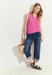 Rosa ärmlös topp med V-hals, blå jeans med uppvikt ärm, och marineblå sandaler, tillsammans med en vävd halmtröja.