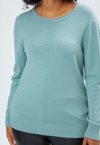 Maglione a maglia azzurro chiaro con scollatura rotonda, orlo a coste e motivo verticale lungo il centro. Materiale morbido, design a maniche lunghe.