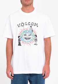 Witte katoenen T-shirt met grafische print van "VOLCOM," puzzelstukken en speelse personages, afgebeeld op een blauw en groen wereldbol ontwerp.