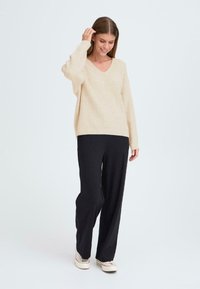 Pull beige en tricot avec un col en V et des manches longues, associé à un pantalon noir ample. Texture lisse, coupe décontractée et design simple.
