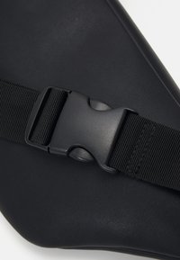 Sac étanche noir avec une finition texturée, doté d'une bandoulière noire ajustable avec une boucle en plastique.