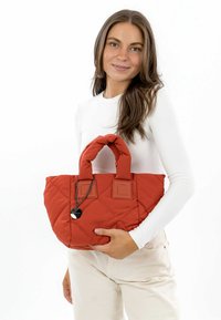 Quilted red bag with two handles and a rectangular shape. Features a metal charm and textured fabric.