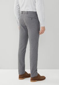 Pantaloni a quadri grigi e bianchi a taglio aderente, con una tasca posteriore, indossati con scarpe in pelle scamosciata marrone e una camicia leggera con bottoni.