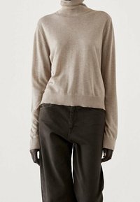 Beige coltrui in zachte stof, aansluitend bij de taille en los in de mouwen, gecombineerd met donkergroene wijde broek.
