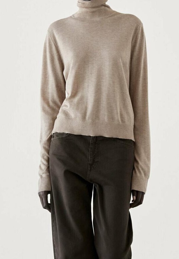 Beige coltrui in zachte stof, aansluitend bij de taille en los in de mouwen, gecombineerd met donkergroene wijde broek.