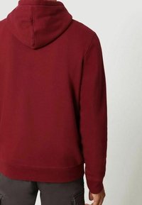 Sudadera color marrón oscuro con capucha ajustable, puños y dobladillo acanalados; hecha de una tela suave, con una textura lisa y un ajuste relajado.