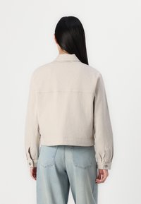 Veste en velours côtelé beige clair à la silhouette courte, grand col et poignets boutonnés, associée à un jean taille haute bleu clair.