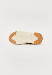 Suola della scarpa caratterizzata da una intersuola bianca texturizzata con uno strato esterno marrone. Il design include indentazioni geometriche per una migliore trazione.