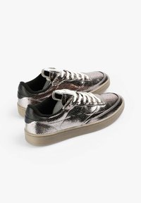 Zapatillas plateadas metálicas con un acabado texturizado, forro de tela negra, cordones planos y suela de goma beige.