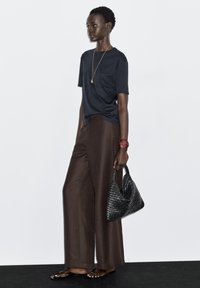 Sort kortærmet T-shirt parret med løse brune vidde benbukser. Tilbehør med en vævet sort taske og rød armbånd. Simpelt design.