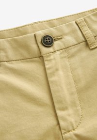 Chinos en coton beige avec fermeture à bouton et passants de ceinture. Présente une texture lisse et des coutures soignées le long des coutures.
