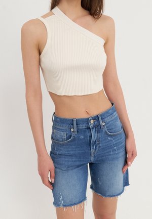 Kremowy prążkowany crop top na jedno ramię, zestawiony z niebieskimi szortami dżinsowymi o średnim stanie z postrzępionym końcem i przetarciami.