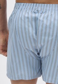 Kék csíkos rövidnadrág könnyű anyagból, keskeny függőleges csíkokkal tengerészkék és fehér színben. Rugalmassal ellátott derékrész és oldalsó varrások láthatók.