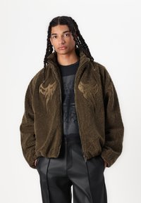 Olivgrön fleecejacka med hög krage och dragkedja, med strukturerad tyg och abstrakt broderi fram.
