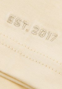 Beige cotton fabric with embroidered text "EST. 2017," featuring a smooth texture and neat stitching along the edge.