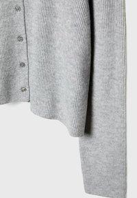 Cardigan grigio a coste realizzato in materiale morbido, con chiusura a bottoni e un design fluido con un orlo leggermente curvo.