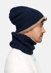 Navy knitted beanie with a textured finish, featuring a beige faux fur lining, paired with a matching knitted neck warmer.