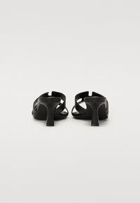 Sorte høye hæler med åpen tå-design, buede stropper og midt-høy stiletto hæl for bedre stabilitet. Jevn tekstur.