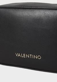 Pochette en cuir noir avec une finition texturée, ornée de lettres dorées "VALENTINO" en bas. Forme rectangulaire, bords lisses.