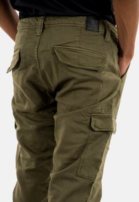 Cargo broek van olijfgroen stof met een relaxte pasvorm, voorzien van een aantal zakken, stikselaccenten en een leren label op de tailleband.