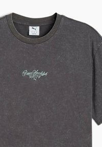 Czarny t-shirt bawełniany w ciemnoszarym kolorze z okrągłym dekoltem i krótkimi rękawami. Z przodu znajduje się haftowane, jasnoniebieskie logo "Puma Sportstyle" na klatce piersiowej.