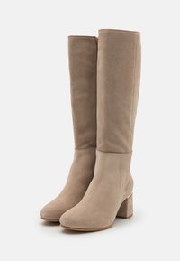 Bottes hautes taupe en suède. Bout carré et talon carré. Texture lisse avec une fermeture éclair sur le côté et un subtil accent métallique.