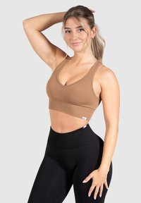 Bruine geribde sportbeha met een V-halsontwerp, gecombineerd met hoge zwarte leggings. Zacht materiaal en naadloze constructie zichtbaar.