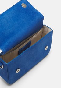 Niebieska skórzana prostokątna torebka z zamknięciem na magnes i beżową podszewką. Wnętrze zawiera kieszonkę na karty. Gładkie wykończenie.